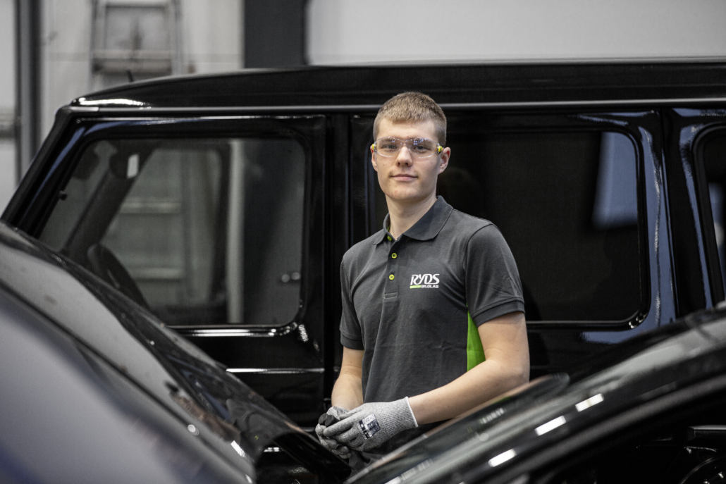 En anställd man hos Ryds bilglas står mellan 2 bilar och tittar in i kameran